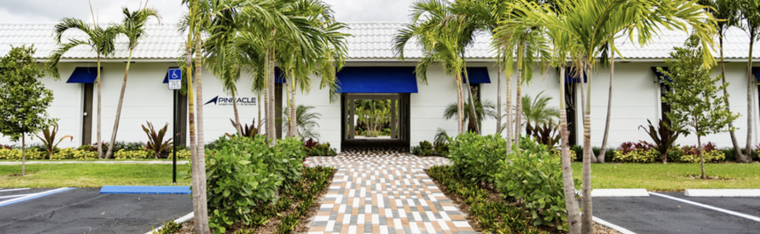 Outside view of Fort Lauderdale Medical Injury Center: Easy Reach Chiropractic's Office Building. Entrance has a blue canopy over door with a long path of pavers surrounded by palm trees and lush green foliage